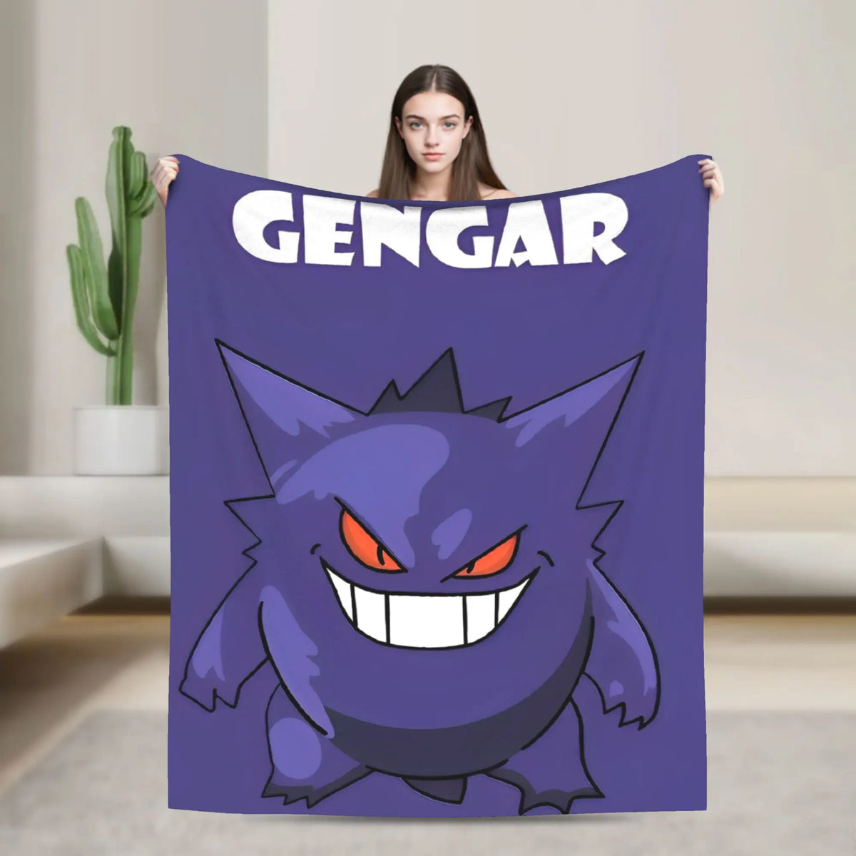 A woman holds up a purple blanket featuring a cartoon Gengar graphic and the word 'GENGAR' in white. The background shows a modern, minimalist living room with a cactus in the distance.