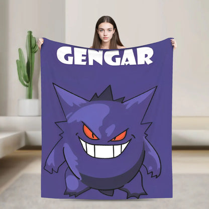 A woman holds up a purple blanket featuring a cartoon Gengar graphic and the word 'GENGAR' in white. The background shows a modern, minimalist living room with a cactus in the distance.