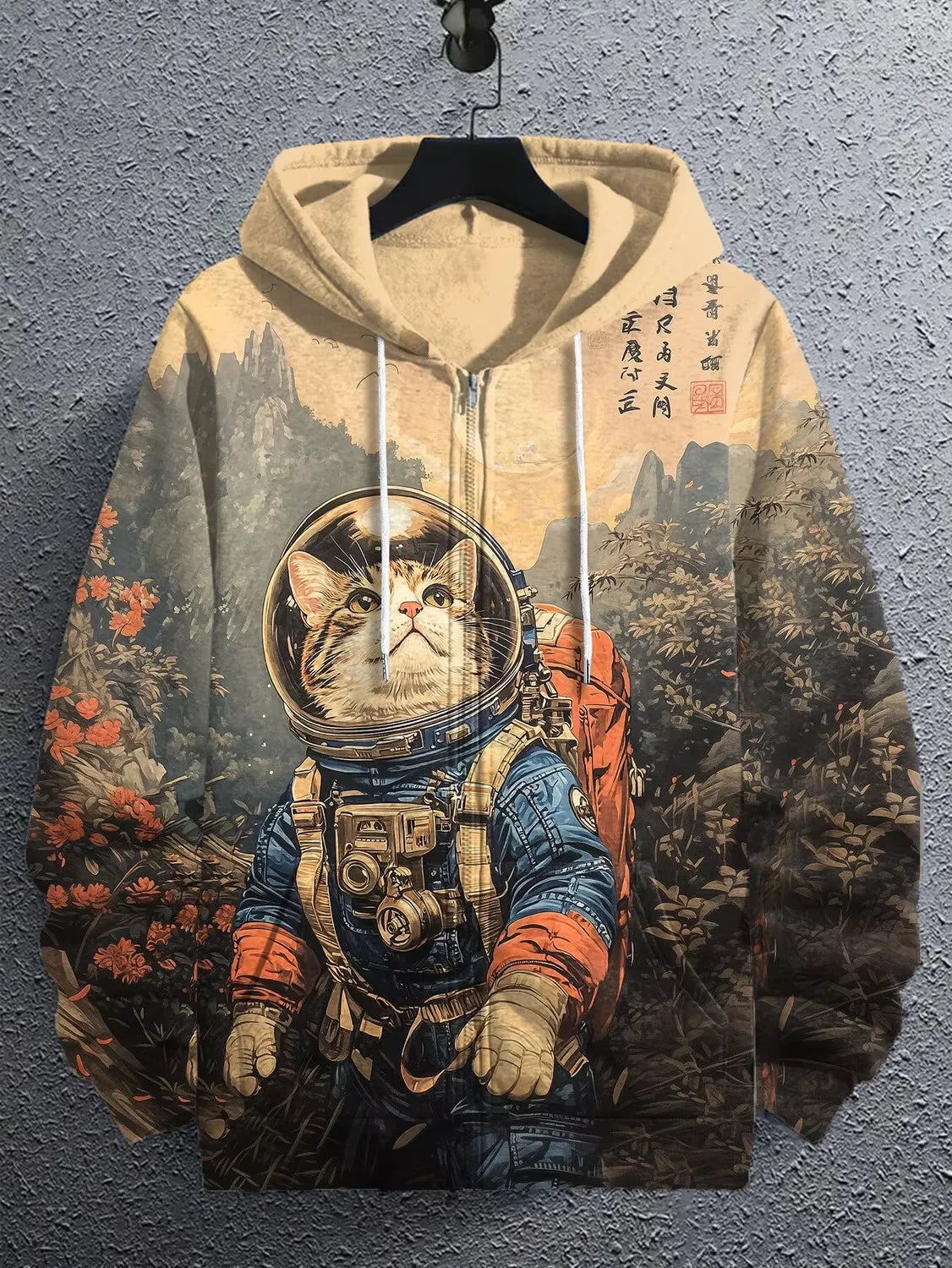 A beige pullover hoodie with a detailed graphic print of a cat in a spacesuit, hanging on a black hanger against a textured gray wall.