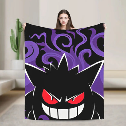 A woman holds up a large blanket or tapestry featuring a stylized black cartoon monster face with red eyes and white teeth, set against a purple swirling background. The product is shown in a modern indoor room setting with a cactus in the background.