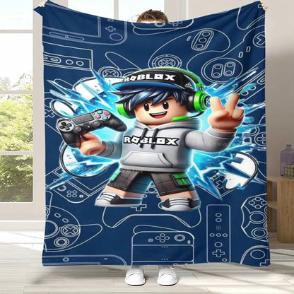 A person holds up a large blue Roblox-themed blanket or tapestry in a bright room. The blanket features a large cartoon Roblox character in the center, wearing a white hoodie, black cap, and green headphones, surrounded by blue electric effects and white game controller outlines.