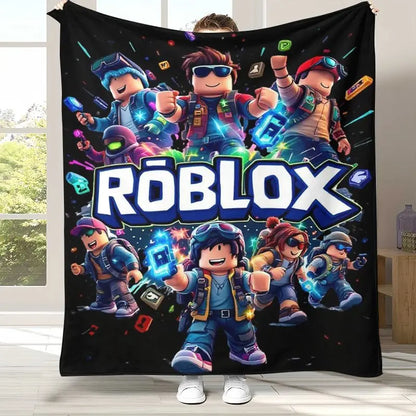 A person holds up a large black Roblox-themed blanket or poster in a bright room. The printed design features multiple colorful Roblox avatar characters and a large 'RØBLOX' logo across the center.