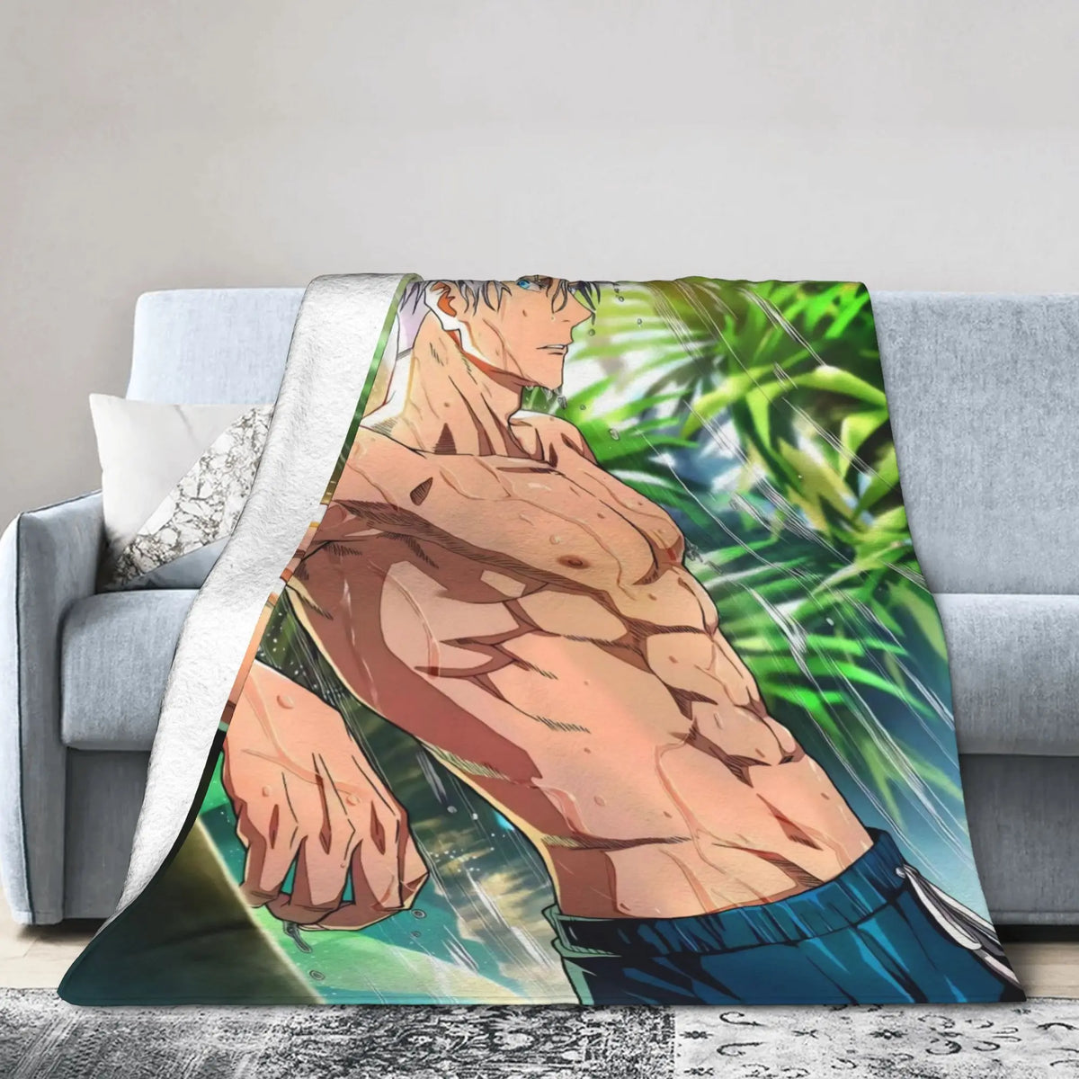 A printed throw blanket draped over a light gray sofa in a living room setting, featuring an anime-style illustration of a shirtless muscular man with green foliage in the background.
