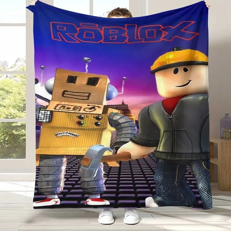 A person holds up a large Roblox-themed wall tapestry or blanket in a room. The printed design shows the Roblox logo at the top, a gold robot on the left, and a Roblox worker character on the right, with a purple-to-pink sky background.