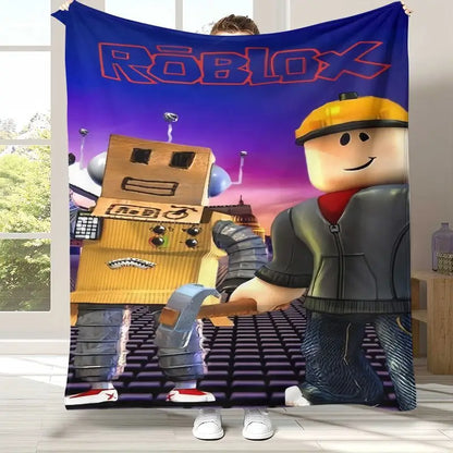 A person holds up a large Roblox-themed wall tapestry or blanket in a room. The printed design shows the Roblox logo at the top, a gold robot on the left, and a Roblox worker character on the right, with a purple-to-pink sky background.