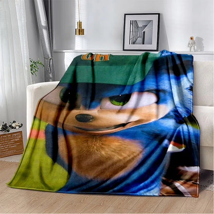 A fleece throw blanket draped over a white sofa in a bright living room. The blanket features a large printed graphic of Sonic the Hedgehog's face with blue, green, orange, and black tones.
