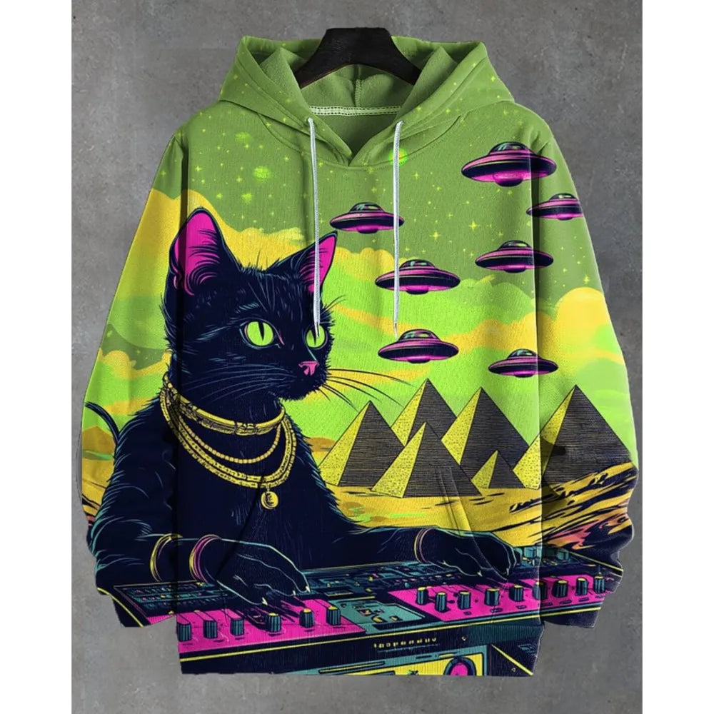 A green pullover hoodie featuring a vibrant graphic print of a black cat playing a keyboard in a desert setting with pyramids, neon pink and yellow elements, and purple flying saucers in the sky. The hoodie is displayed on a black hanger against a textured gray background.