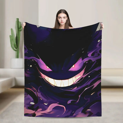 A woman holds up a large square wall tapestry featuring a stylized, dark purple and black cartoon monster face with glowing pink eyes and a wide grin. The tapestry is displayed in a modern, minimalist room with a cactus in the background.