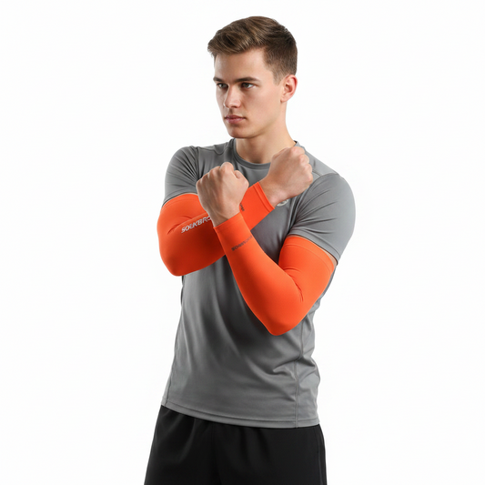 A man wearing a gray athletic t-shirt and black shorts, demonstrating a pair of bright orange arm warmers on his forearms against a solid white background.