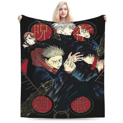 A person holds up a large black blanket or throw featuring anime-style characters and red circular motifs. The blanket is shown against a plain white studio background, with the model's hands and lower body visible behind it.