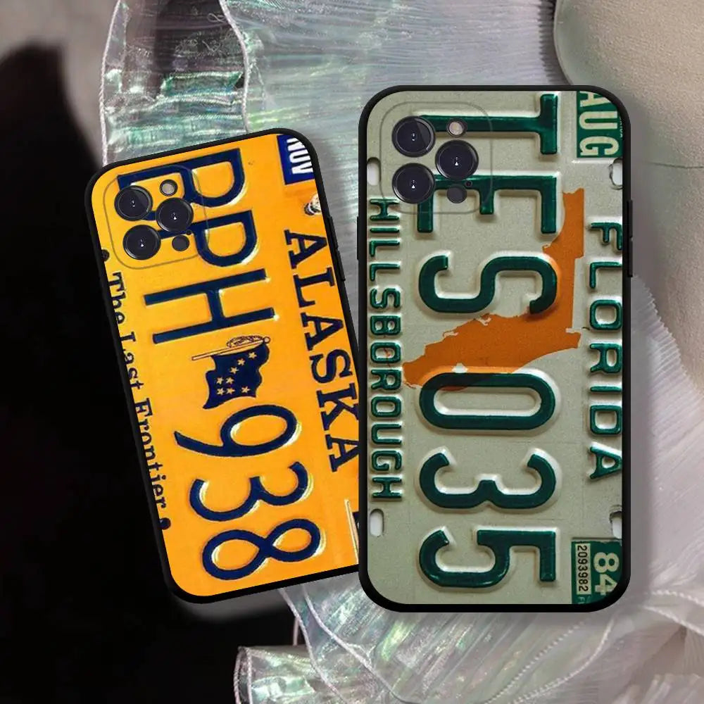 Two phone cases featuring vintage license plate designs, one yellow and blue with Alaska plate styling, and one beige and green with Florida plate styling, displayed on a crinkled iridescent sheet.