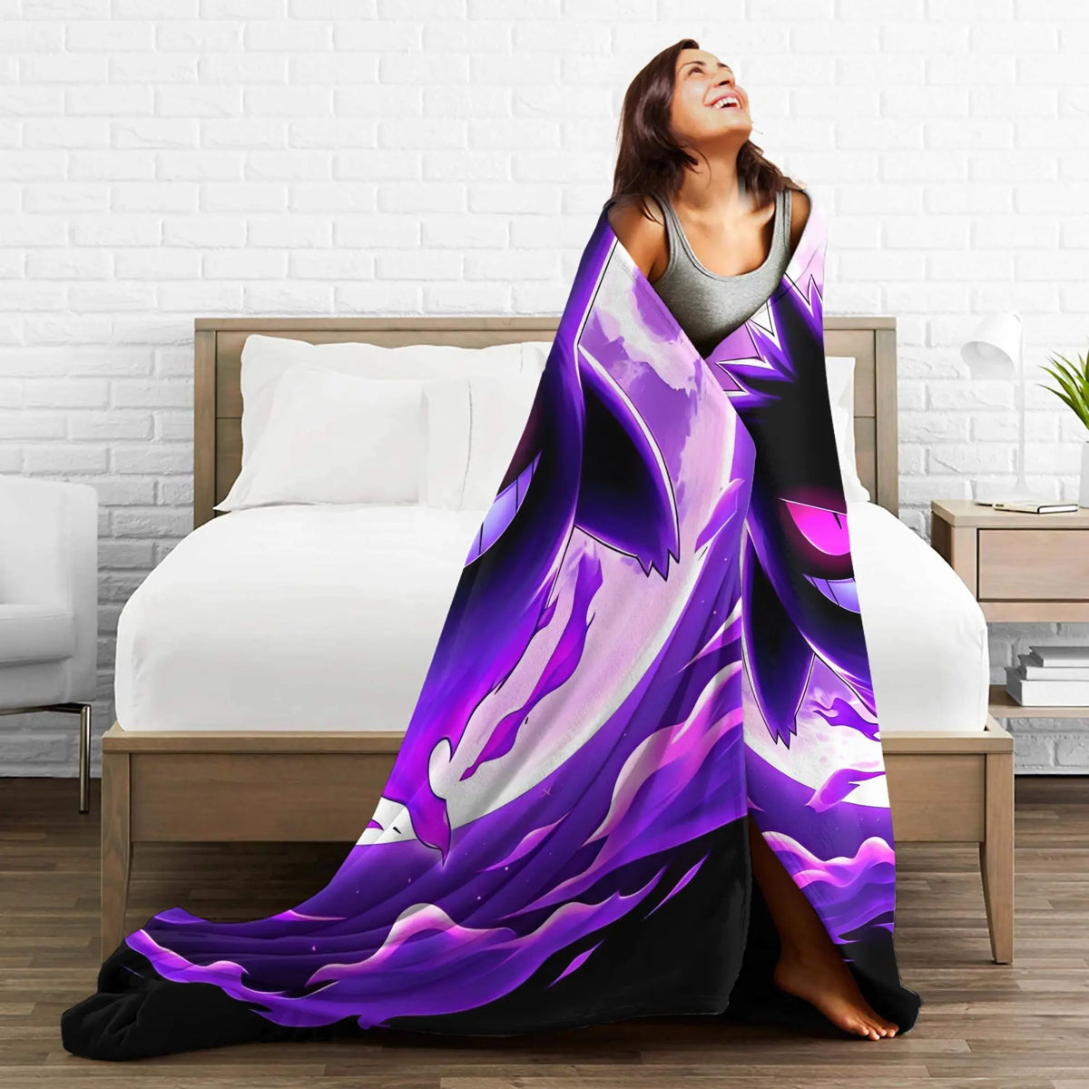 A woman wrapped in a large purple and black abstract blanket standing in front of a bed in a modern bedroom setting.