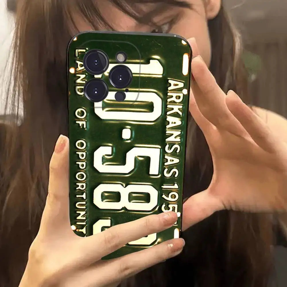 A person holding a phone case featuring a vintage Arkansas license plate design with the text 'ARKANSAS 1957' and 'LAND OF OPPORTUNITY' in white on a dark green background.