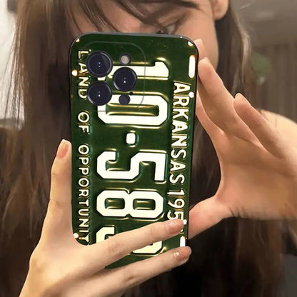 A person holding a phone case featuring a vintage Arkansas license plate design with the text 'ARKANSAS 1957' and 'LAND OF OPPORTUNITY' in white on a dark green background.