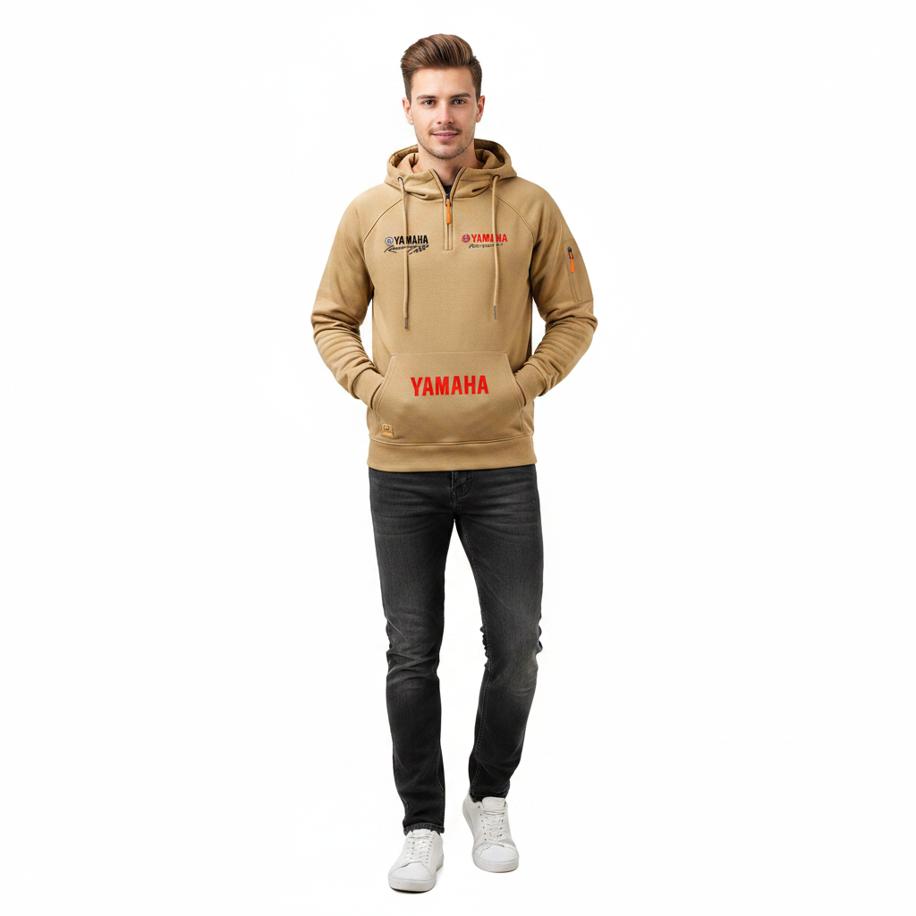 A man modeling a tan half-zip hoodie with 'YAMAHA' printed in red on the front and black graphics on the left chest, paired with dark gray jeans and white sneakers, against a plain white background.