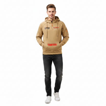 A man modeling a tan half-zip hoodie with 'YAMAHA' printed in red on the front and black graphics on the left chest, paired with dark gray jeans and white sneakers, against a plain white background.