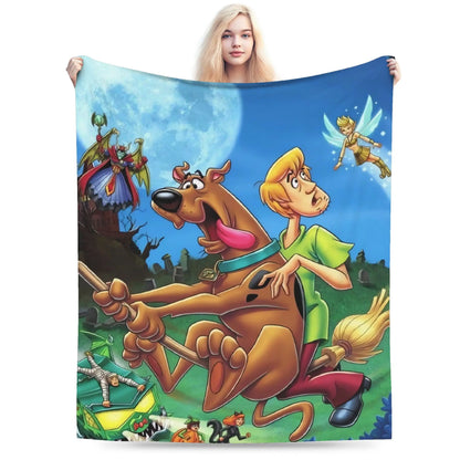 A person holds up a large printed blanket or tapestry featuring cartoon characters from Scooby-Doo, including Scooby-Doo, Shag, and a fairy, against a plain white background.