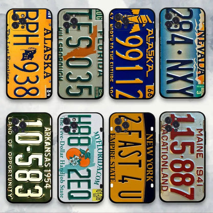 Eight phone cases designed to look like vintage US license plates, arranged in a 2x4 grid on a light marble background. The designs include states such as Alaska, Florida, Nevada, Arizona, New York, Maine, and others, featuring colorful retro patterns and text.
