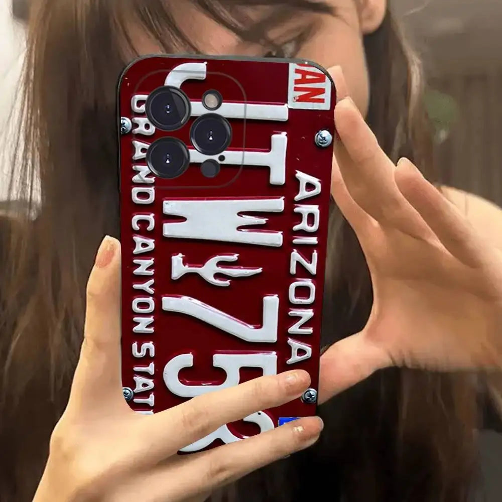 A close-up of a person holding a red Arizona license plate phone case in front of their face, showing the case design with white lettering and silver screws.