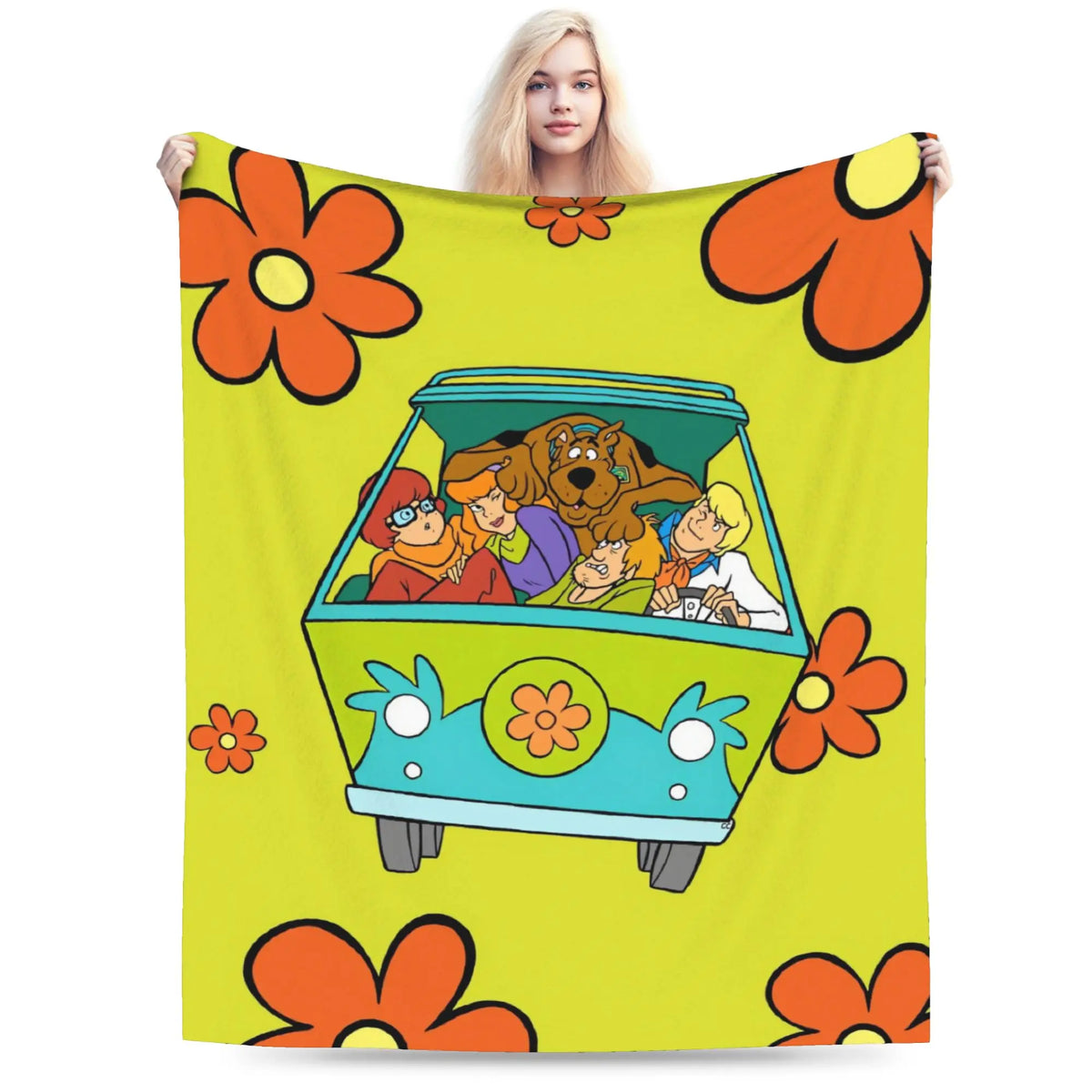 A person holds up a large blanket featuring a retro 1960s-style floral pattern and a cartoon van with characters inside, shown against a plain white background.