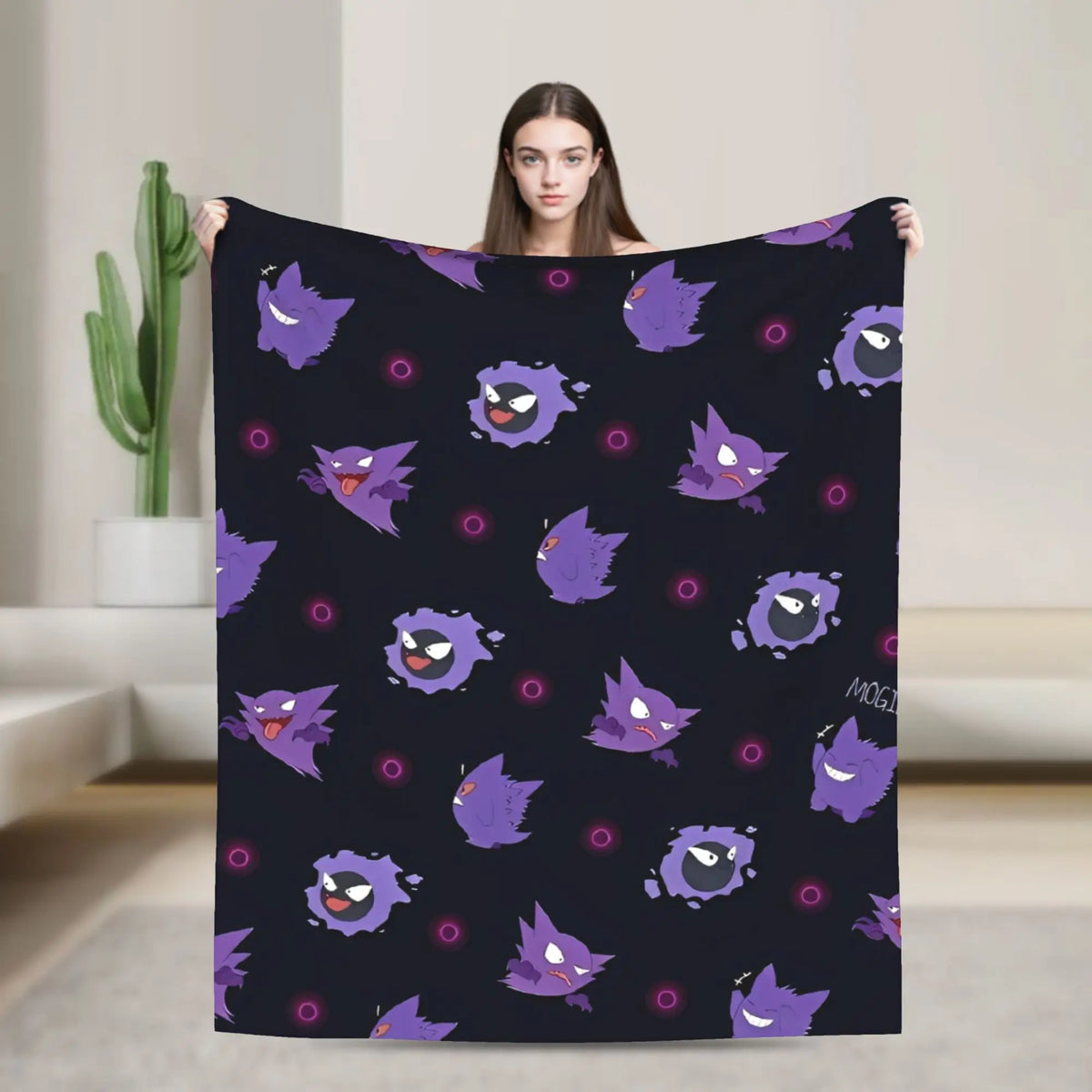 A woman holds up a black blanket featuring a repeating pattern of purple cartoon ghosts, with a neutral indoor background.