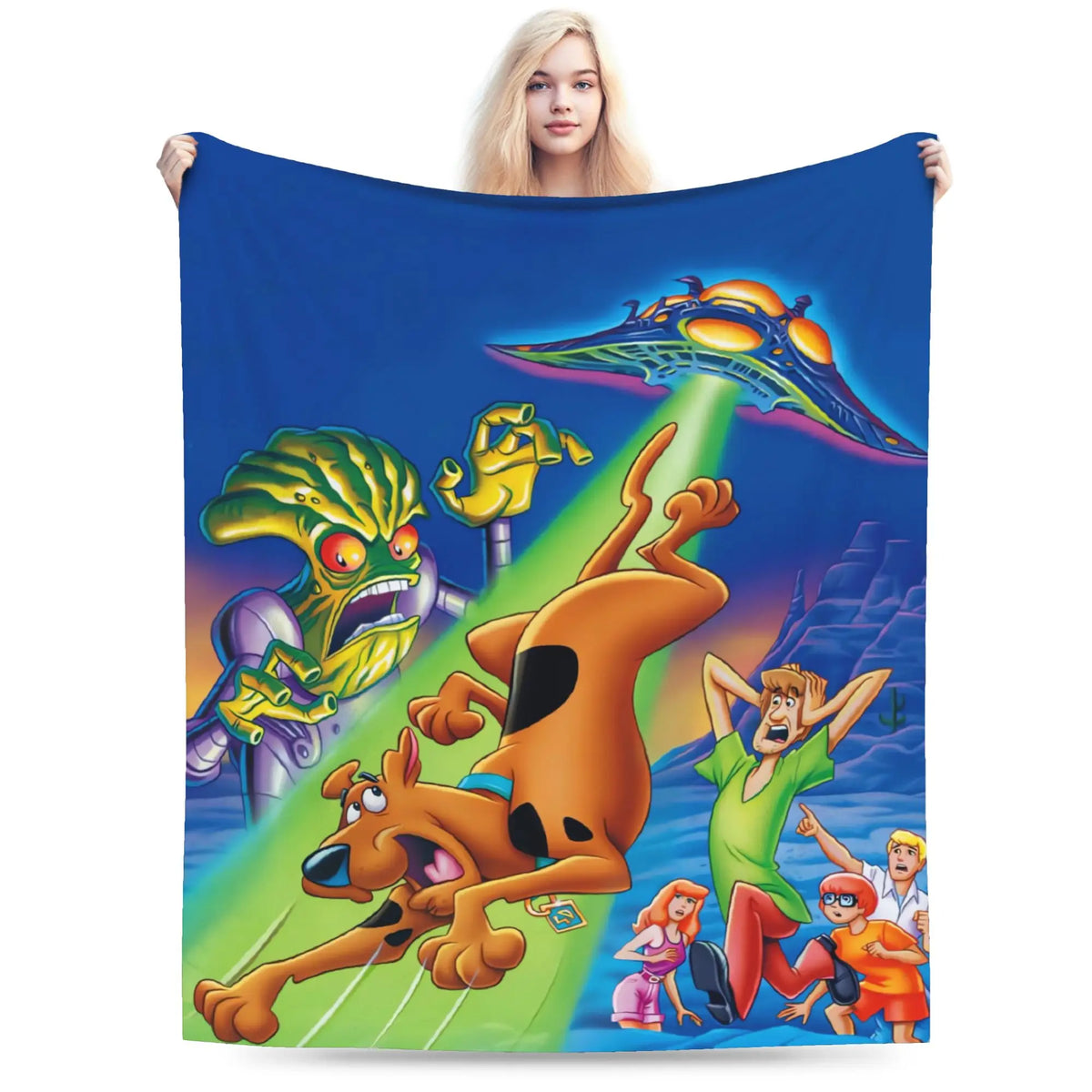 A person holds up a large printed blanket or tapestry featuring the Scooby-Doo cartoon scene against a plain white studio background. The blanket shows Scooby, Shag, Fred, Velma, and the Mystery Machine in bright colors.