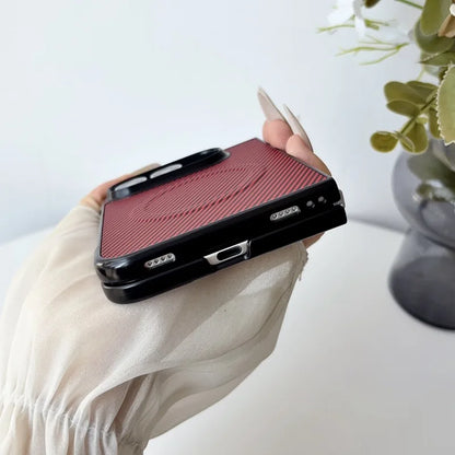 A hand wearing a cream-colored sleeve holds a black phone case with a textured red backplate featuring a circular magnetic design, set against a bright, softly blurred background with a plant in a vase.
