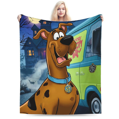 A person holds up a large printed blanket or tapestry featuring Scooby-Doo standing in front of a haunted house and a green-and-blue Mystery Van. Because a person is visible holding the item, the subject_type is classified as Lifestyle.
