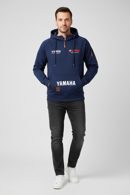 A man modeling a navy blue hoodie with 'YAMAHA' printed in white across the front pocket, paired with dark gray jeans and white sneakers, against a light gray studio background.