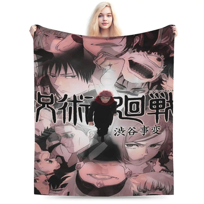 A person holding up a large printed blanket or tapestry featuring anime-style character artwork and Japanese text. The blanket has a collage of illustrated faces and figures in muted pink, black, gray, and beige tones, with a small red-haired character near the center.