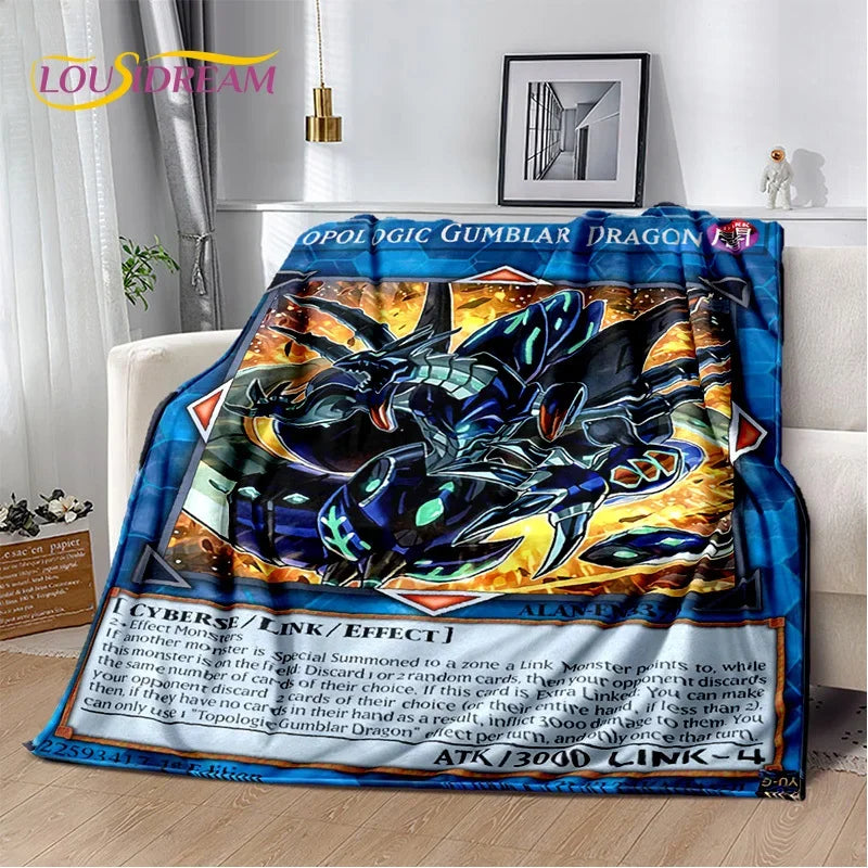 A plush throw blanket featuring a detailed Yu-Gi-Oh! card illustration of Opal the Gumbler Dragon, draped over a white sofa in a living room setting.