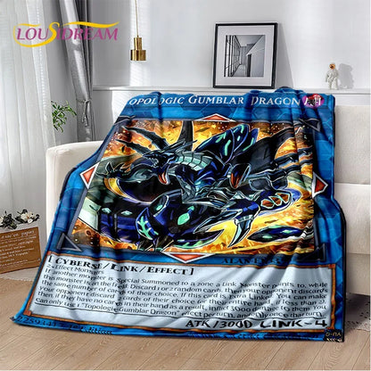 A plush throw blanket featuring a detailed Yu-Gi-Oh! card illustration of Opal the Gumbler Dragon, draped over a white sofa in a living room setting.