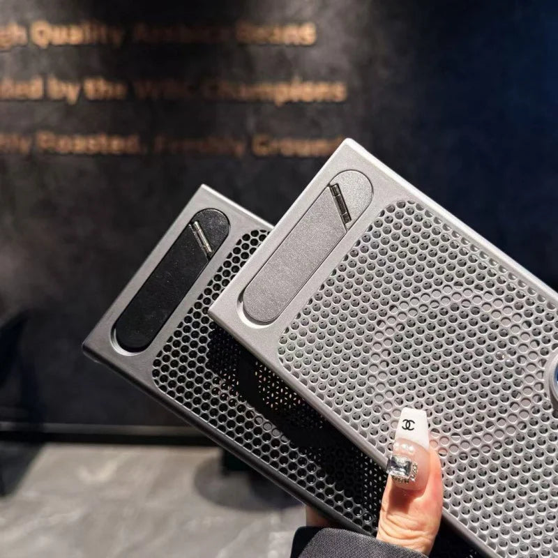 Two gray metal boxes with honeycomb patterns held by a hand against a dark background.