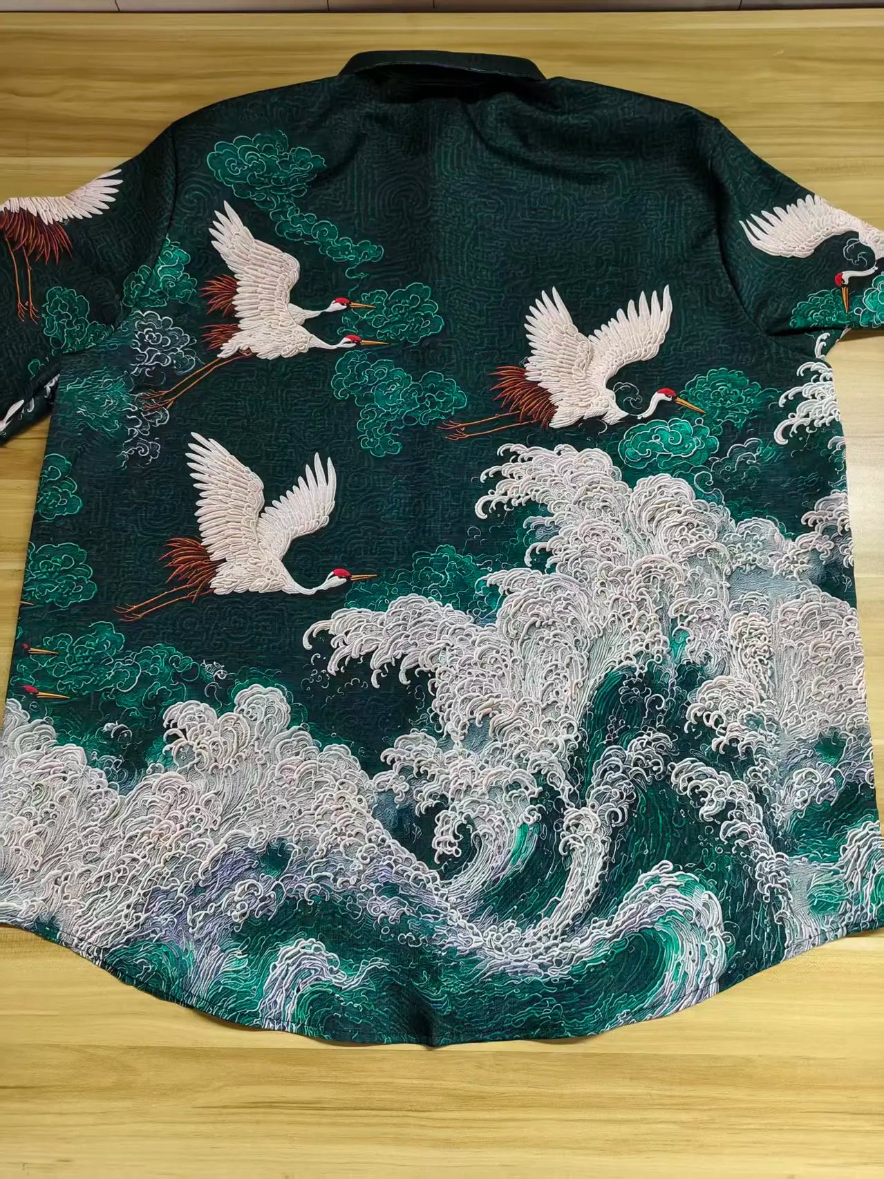Embroidered garment with cranes and wave design on a wooden surface