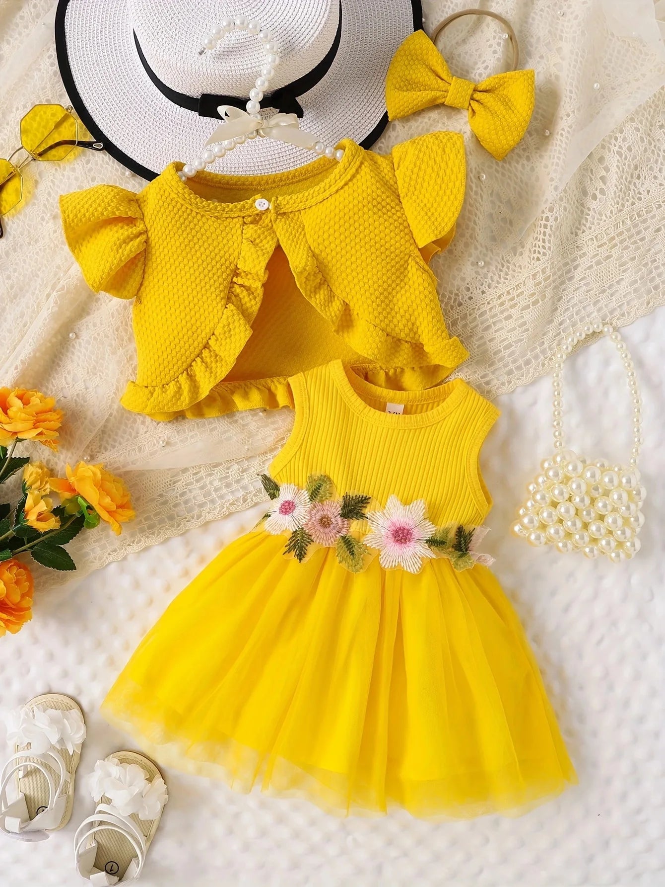Yellow dress with floral details, matching cardigan, and accessories on a textured surface.