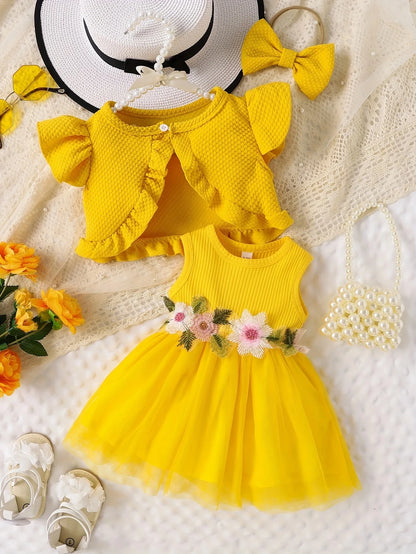 Yellow dress with floral details, matching cardigan, and accessories on a textured surface.