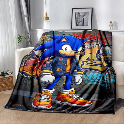 A fleece throw blanket featuring a large graphic print of Sonic the Hedgehog standing in front of graffiti-style city walls, draped over a white sofa in a living room setting.