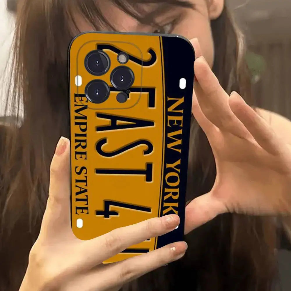A close-up of a person holding a smartphone case in front of their face. The case is designed to look like a yellow and black New York Empire State license plate with the text 'EMPIRE STATE' and 'NEW YORK'.