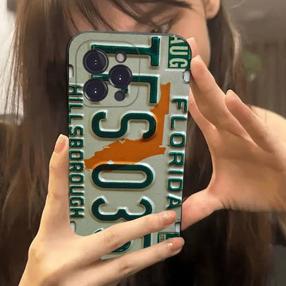 A phone case featuring a Florida license plate design with 'Tampa' and 'Orange' elements, held up in a mirror selfie by a person.