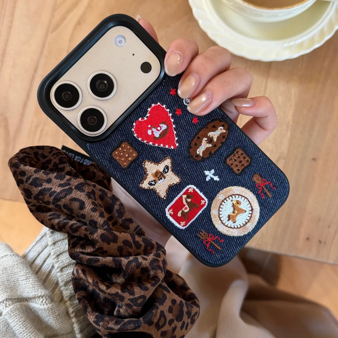 Phone case with embroidered designs held by a person on a wooden surface