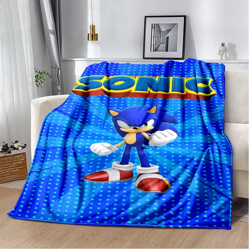 A blue throw blanket featuring Sonic the Hedgehog printed on the front, draped over a white sofa in a modern living room setting.