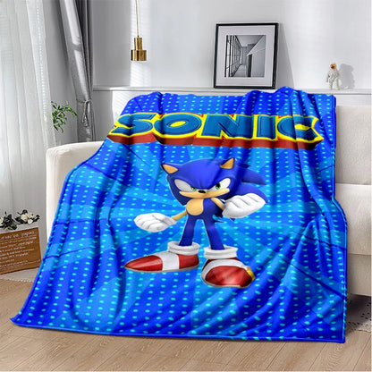 A blue throw blanket featuring Sonic the Hedgehog printed on the front, draped over a white sofa in a modern living room setting.