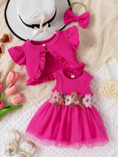 Pink children's dress with floral details, matching headband, and white hat on a textured surface.