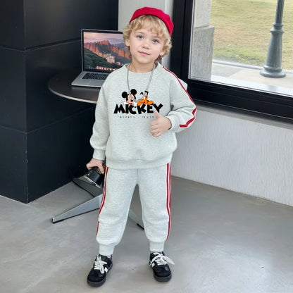 Child wearing a gray Mickey Mouse outfit standing indoors with a laptop on a desk.
