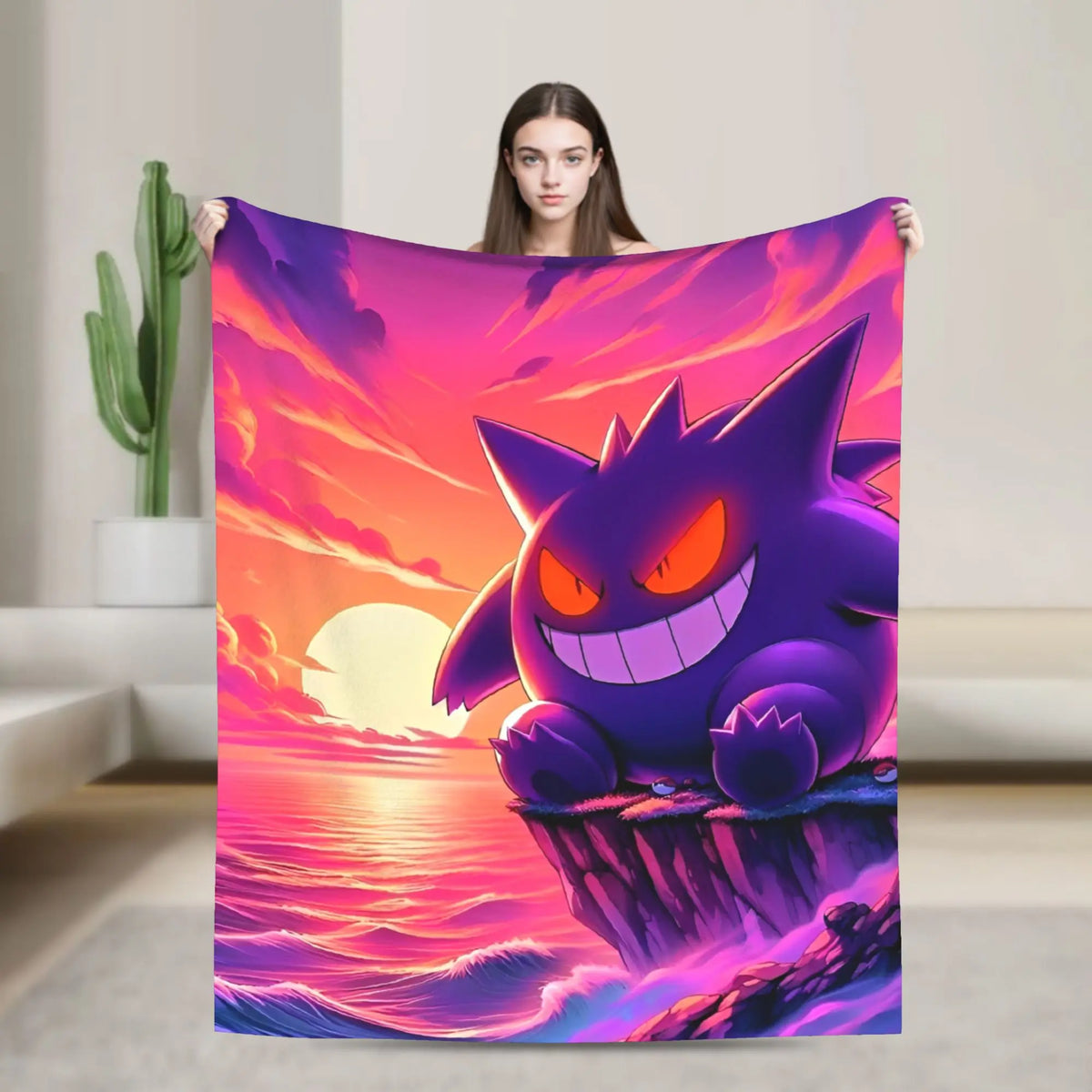 A woman holds up a large blanket or tapestry featuring a stylized purple cartoon creature on a pink and orange sunset seascape. The product is shown in a real indoor room with a cactus and wall visible, so this is Lifestyle rather than Product/Packaging.