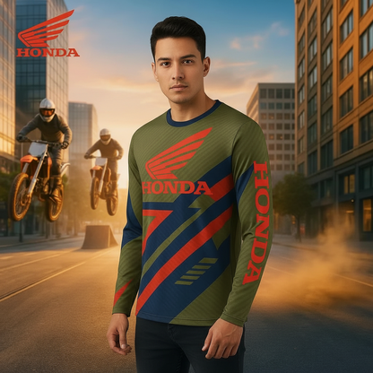 A man wearing a long-sleeve Honda performance jersey stands in an urban street scene at sunset, with motorcycle riders visible in the background. The jersey is olive green with bold red and navy graphic panels and large Honda wing and wordmark graphics.