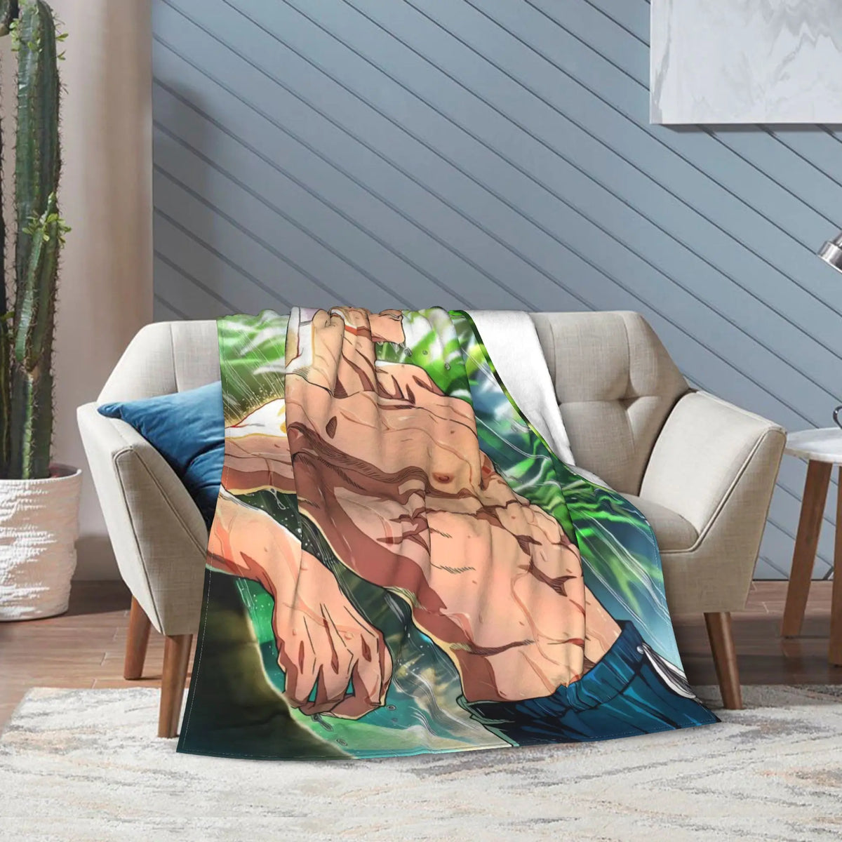 A printed throw blanket draped over a beige armchair in a styled living room. The blanket features a large anime-style illustration of a shirtless man with blue pants against a green tropical background.