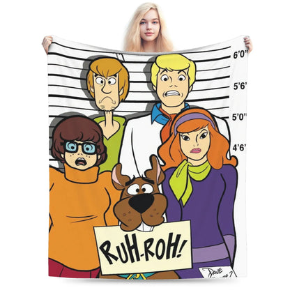 A person holds up a large printed blanket or tapestry featuring a cartoon group portrait of Scooby-Doo characters against a white background with height markings. Because a person is visible holding the item, the subject_type is classified as Lifestyle.