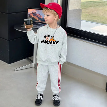 Child wearing a Mickey Mouse sweatshirt in an indoor setting with a laptop on a desk.
