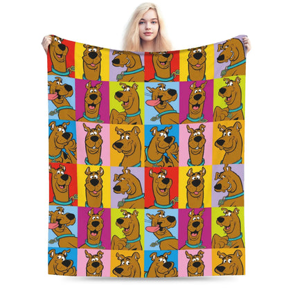 A person holds up a large blanket featuring a colorful grid pattern of Scooby-Doo cartoon faces on a plain white background.